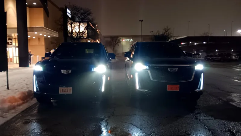 Two black Cadillac Escalades with headlights on at night