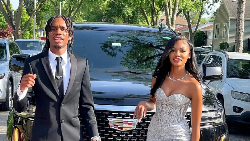 Prom couple posing in front of a black Cadillac Escalade